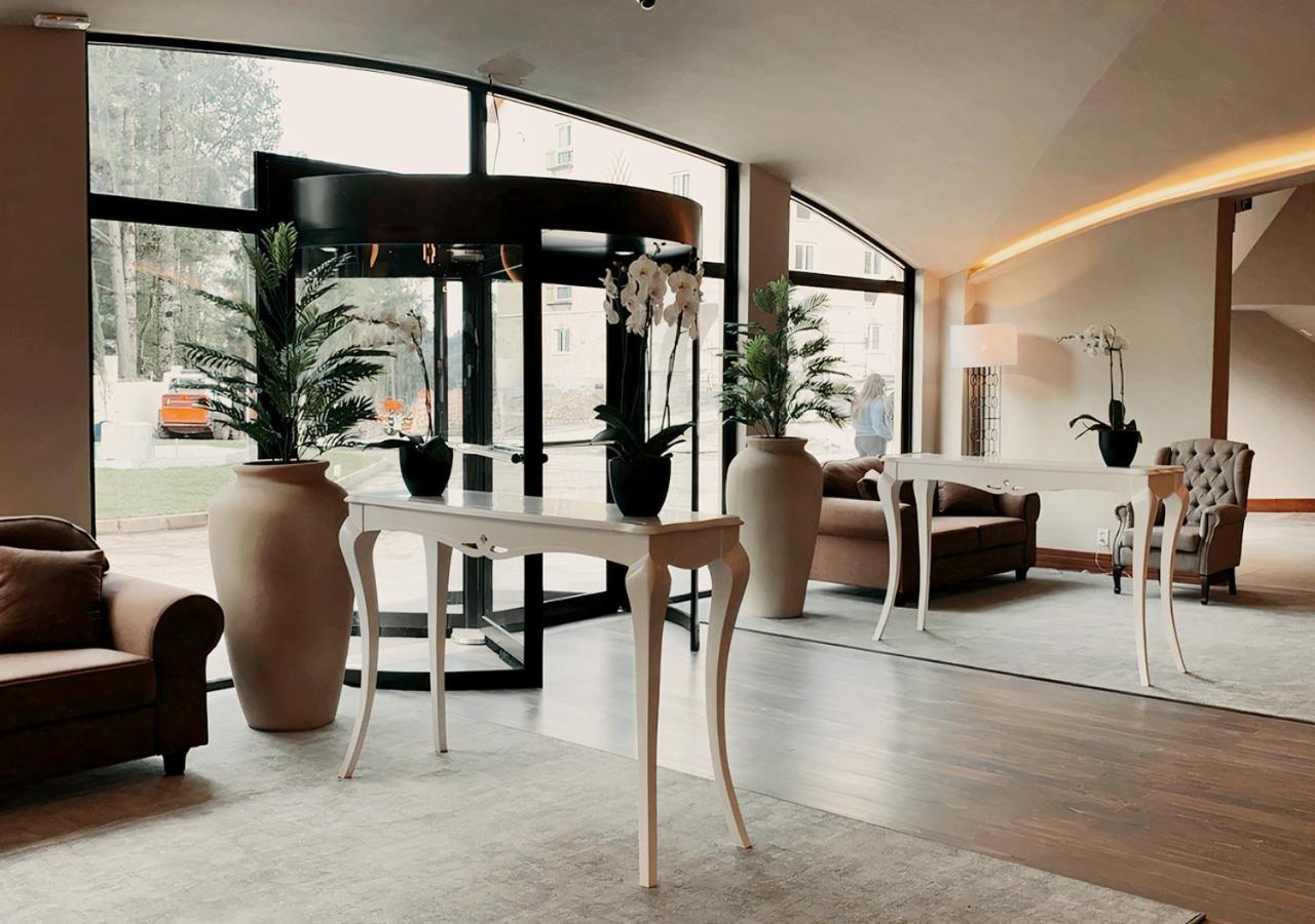 Buona Vitta Gramado Resort & Spa By Gramado Parks Exterior foto The photo displays an elegant interior space, likely a hotel or a high-end lobby. In the foreground, there is a stylish table with a curved design, positioned near large glass doors leading outside. Flanking the table are two large planters with lush