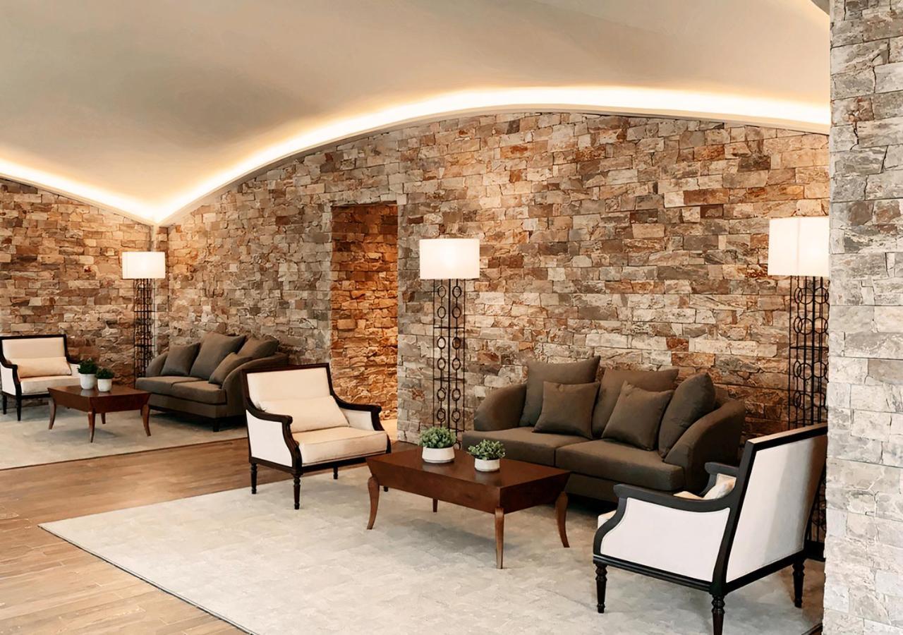 Buona Vitta Gramado Resort & Spa By Gramado Parks Exterior foto The photo shows a stylish and modern lounge area. The walls are made of natural stone, creating a warm and inviting atmosphere. There are two comfortable sofas in a muted gray color arranged around a wooden coffee table. Flanking the sofas are elegan