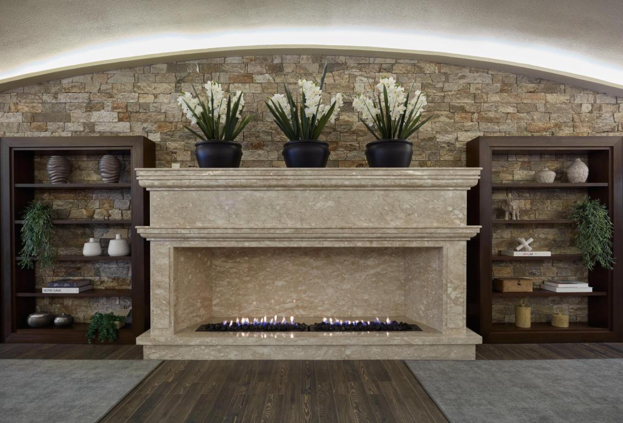 Buona Vitta Gramado Resort & Spa By Gramado Parks Exterior foto The photo shows a modern fireplace design built into a wall with a textured stone background. The fireplace is made of a light-colored stone and features a long, narrow gas flame visible at the bottom. Above the fireplace, there are two large potted 