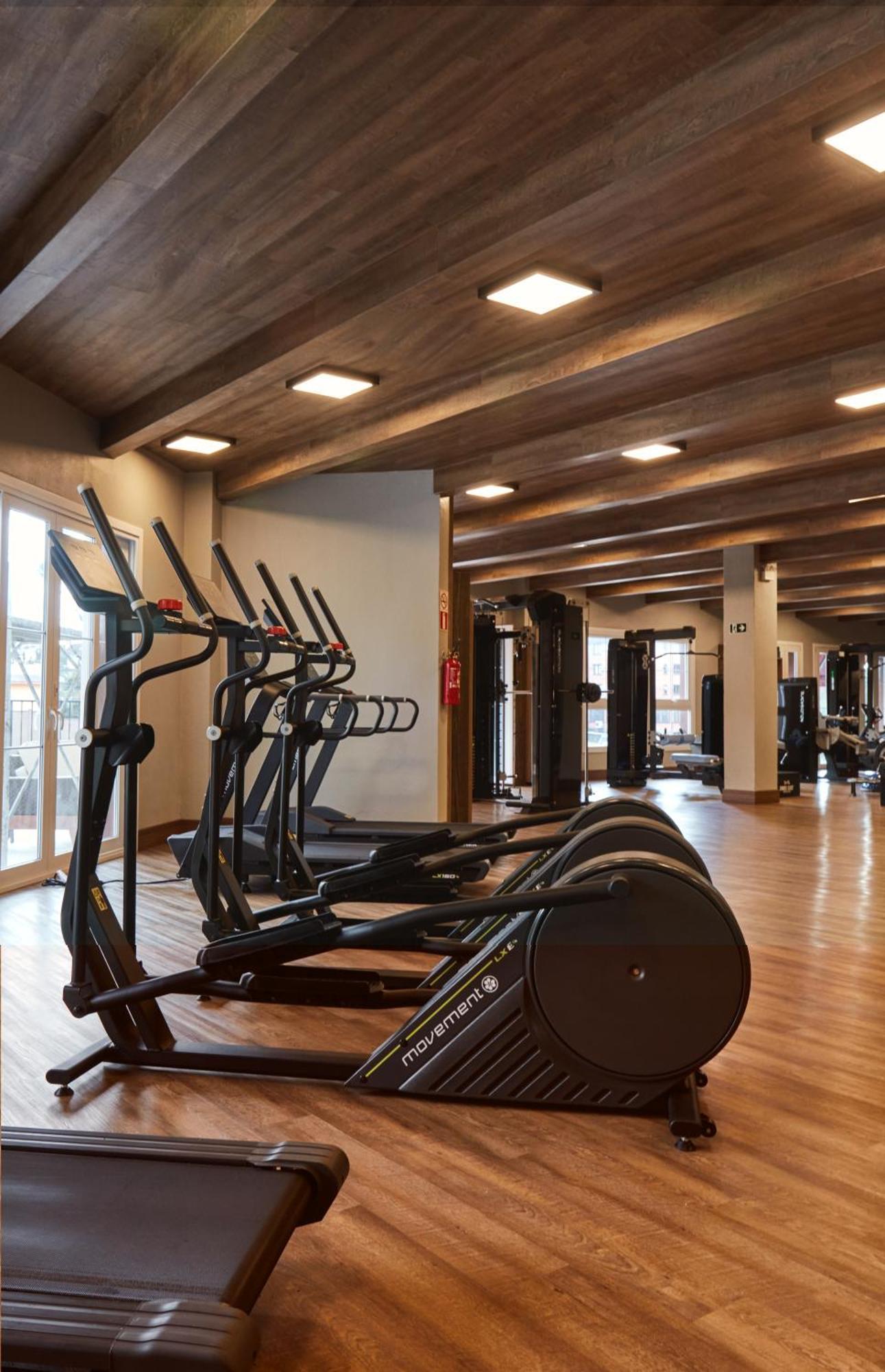 Buona Vitta Gramado Resort & Spa By Gramado Parks Exterior foto The photo shows a modern gym interior with wooden flooring and a ceiling with wooden beams. There are several exercise machines, including elliptical trainers and a treadmill, positioned in the foreground. In the background, there are additional work
