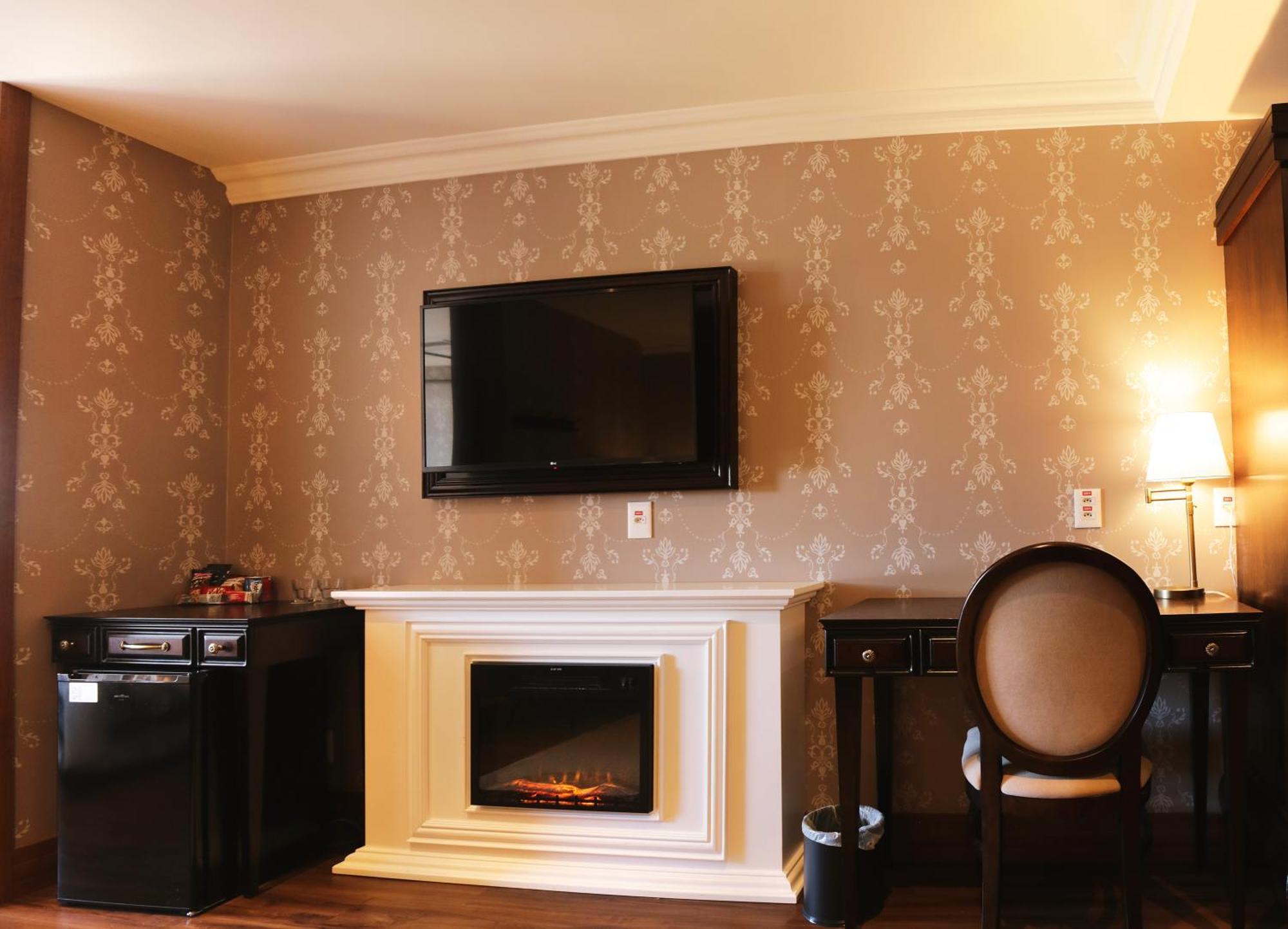 Buona Vitta Gramado Resort & Spa By Gramado Parks Exterior foto The photo shows a cozy room featuring a decorative wall with a subtle pattern. On one side, there is a modern flat-screen television mounted on the wall. Below it, there is a stylish electric fireplace framed in white. Adjacent to the fireplace is a 