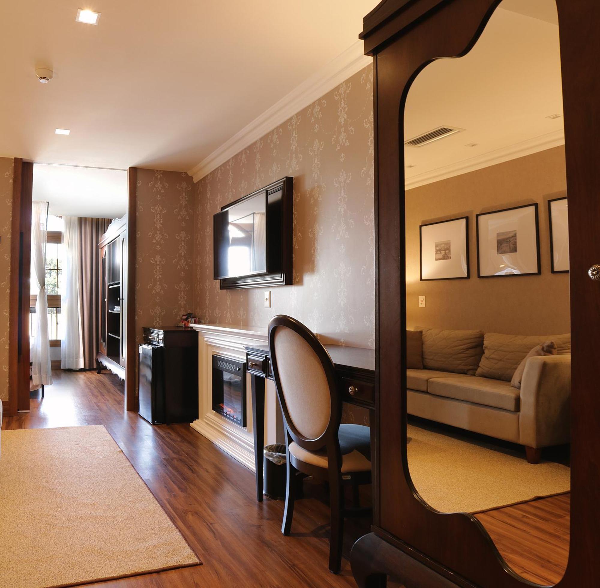 Buona Vitta Gramado Resort & Spa By Gramado Parks Exterior foto The photo shows a well-decorated room that appears to be a living area or a hotel suite. In the foreground, there is a round chair and a desk. A large mirror reflects the living space, creating a sense of spaciousness. 

On the wall is a flat-screen 